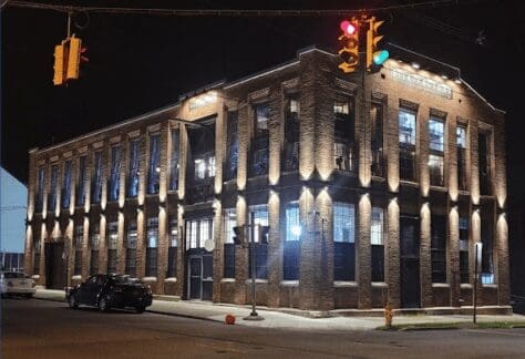 Night view of a The Silk Factory, a well-lit, two-story brick building on a street corner with traffic lights.