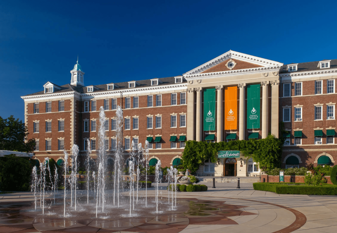 Fountain in front of a large brick building with green banners and a welcoming sign.