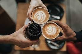 Three hands holding coffee cups with latte art and a glass of iced coffee, viewed from above.