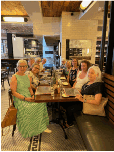 A group of people sit around a long table in a restaurant, looking toward the camera, with menus and drinks on the table.