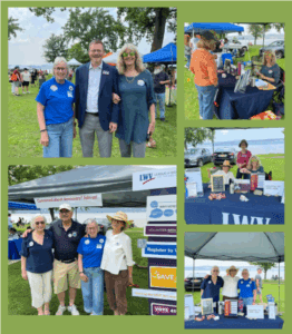 People at an outdoor League of Women Voters event with informational tables, signs, and a park setting in the background.